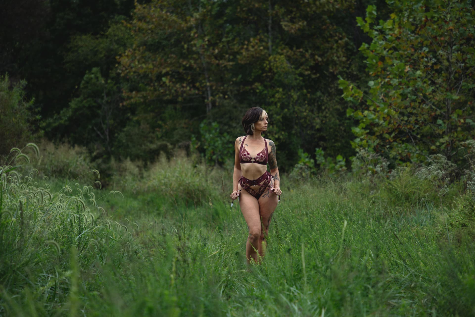 A woman walking confidently through a green field during an on-location River Rose Boudoir session near St. Charles, MO.