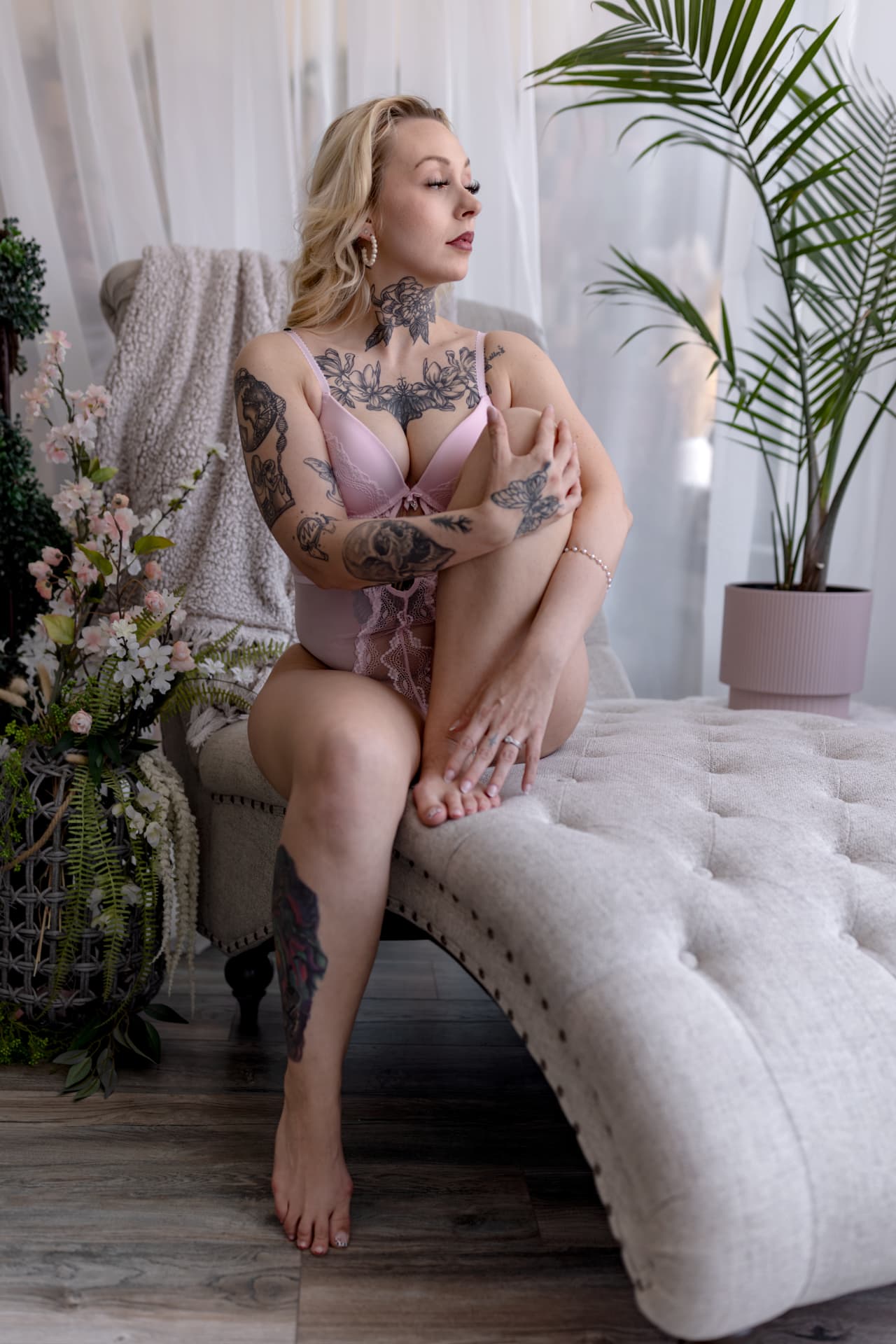 Blonde woman with tattoos in pink lingerie seated on a chaise lounge