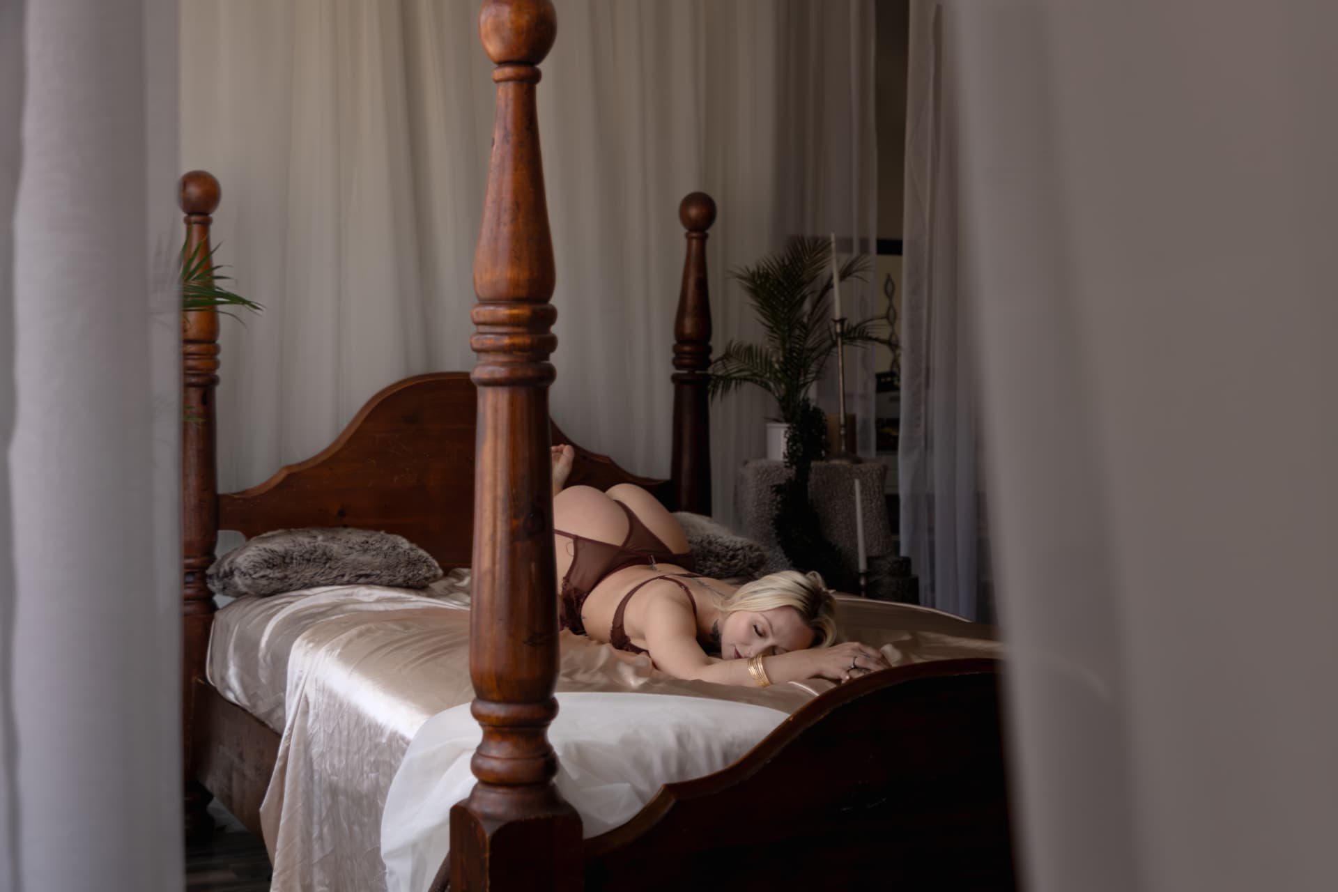 Client resting on a four-poster bed in soft natural light during a boudoir session.